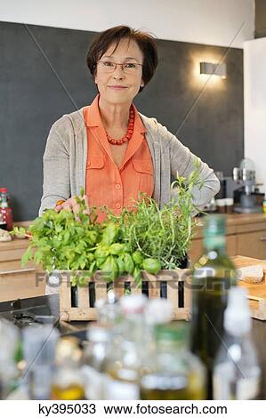 Stock Image - Woman standing in the kitchen with an organic plant. Fotosearch