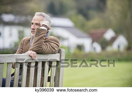 Man sitting on a bench and thinking in a park View Large Photo Image Stock Photo - Man sitting on a bench and thinking in a park. Fotosearch