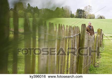 Man standing by fence in a field View Large Photo Image Stock Photograph - Man standing by fence in a field. Fotosearch