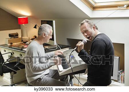 Stock Image - Two male friends playing a piano and singing. Fotosearch
