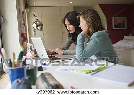 Girl studying with her mother on a laptop at home View Large Photo Image Stock Image - Girl studying with her mother on a laptop at home. Fotosearch