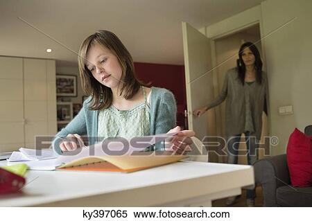 Stock Photography - Girl studying with her mother standing at door in the background. Fotosearch