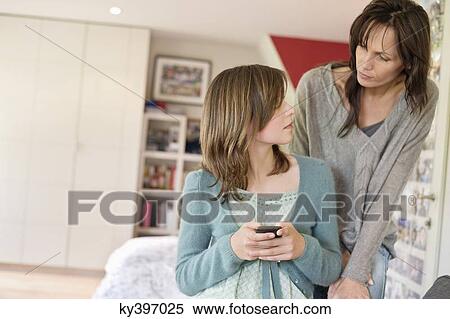 Girl text messaging on mobile phone and looking at her mother View Large Photo Image Stock Photography - Girl text messaging on mobile phone and looking at her mother. Fotosearch