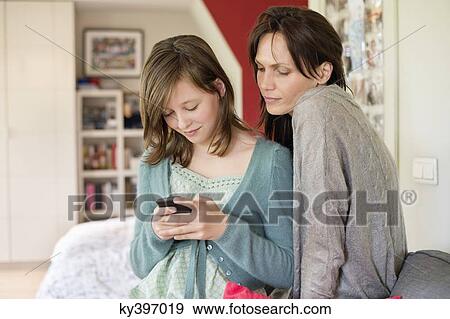 Girl text messaging on mobile phone with her mother at home View Large Photo Image Stock Photo - Girl text messaging on mobile phone with her mother at home. Fotosearch