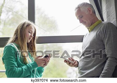 Man and daughter using their mobile phones View Large Photo Image Picture - Man and daughter using their mobile phones. Fotosearch