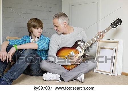 Man playing a guitar with his son at home View Large Photo Image Stock Photo - Man playing a guitar with his son at home. Fotosearch