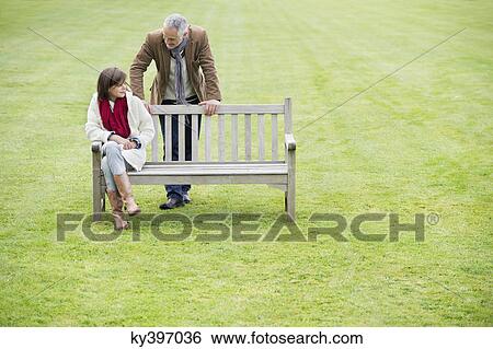 Man sitting with his daughter on a bench in a park View Large Photo Image Stock Photograph - Man sitting with his daughter on a bench in a park. Fotosearch