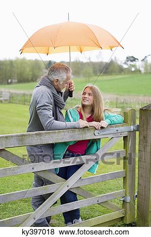 Man standing with his daughter in a farm with an umbrella View Large Photo Image Stock Photo - Man standing with his daughter in a farm with an umbrella. Fotosearch