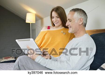 Man using a digital tablet with his daughter at home View Large Photo Image Stock Photograph - Man using a digital tablet with his daughter at home. Fotosearch