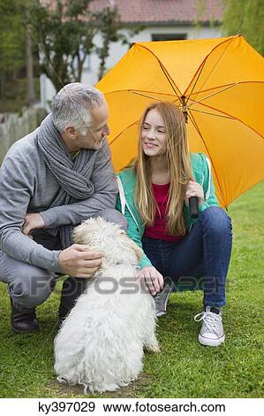 Stock Photo - Man with his daughter pampering a dog in a lawn. Fotosearch