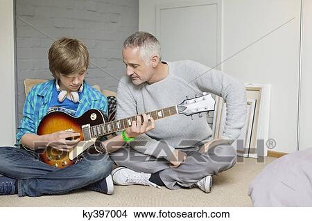Picture - Teenage boy learning guitar with his father at home. Fotosearch