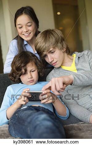 Boy using a cellphone with his brother and sister at home View Large Photo Image Stock Image - Boy using a cellphone with his brother and sister at home. Fotosearch