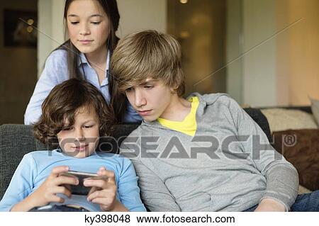 Stock Photo - Boy using a cellphone with his brother and sister at home. Fotosearch