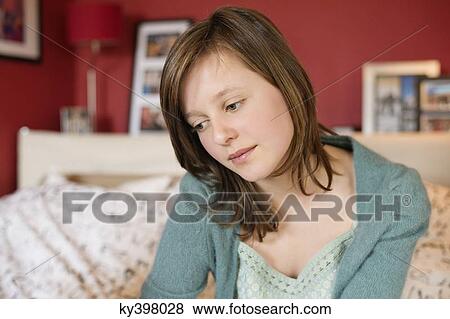 Stock Photo - Girl sitting on the bed and thinking. Fotosearch