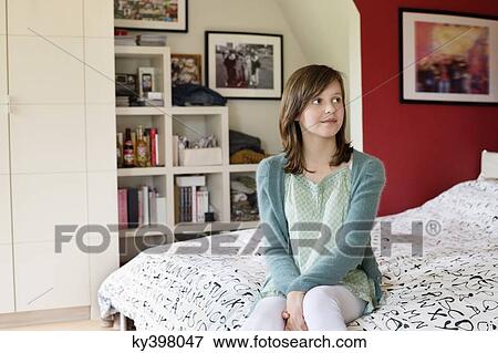 Girl sitting on the bed at home View Large Photo Image Stock Photo - Girl sitting on the bed at home. Fotosearch