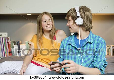 Picture - Teenage boy listening to music on iPod with his sister at home. Fotosearch