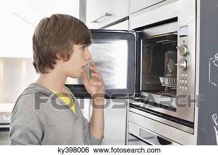 Teenage boy looking into an oven with surprise View Large Photo Image Stock Photograph - Teenage boy looking into an oven with surprise. Fotosearch