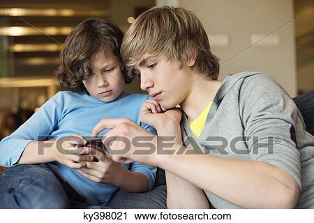 Teenage boy with his brother using a cellphone View Large Photo Image Stock Image - Teenage boy with his brother using a cellphone. Fotosearch