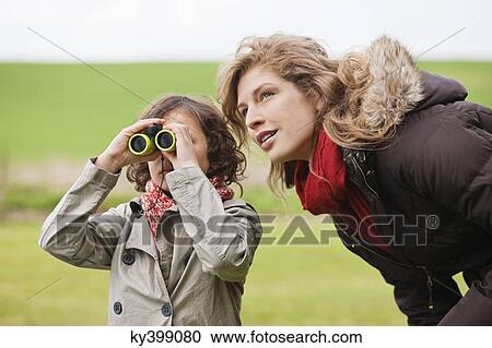 Boy looking through binoculars standing with his mother View Large Photo Image Stock Image - Boy looking through binoculars standing with his mother. Fotosearch