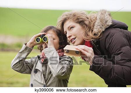 Boy looking through binoculars standing with his mother View Large Photo Image Stock Photograph - Boy looking through binoculars standing with his mother. Fotosearch