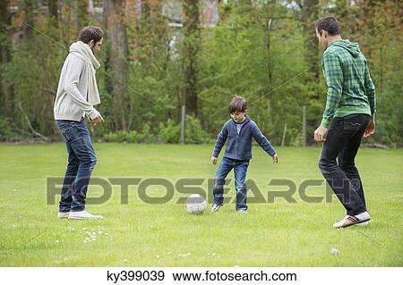 Boy playing soccer with two men in a park View Large Photo Image Stock Photo - Boy playing soccer with two men in a park. Fotosearch