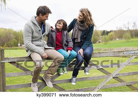 Stock Image - Boy sitting with his parents on the gate of a cottage. Fotosearch