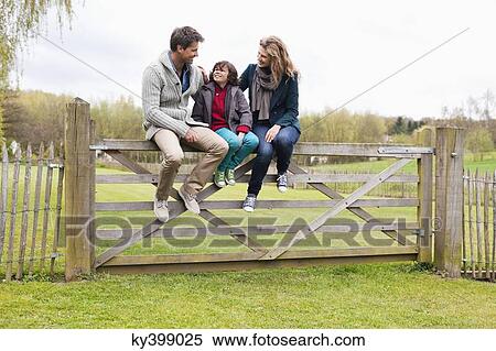 Boy sitting with his parents on the gate of a cottage View Large Photo Image Stock Photography - Boy sitting with his parents on the gate of a cottage. Fotosearch