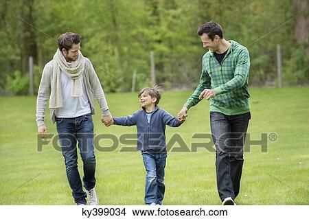 Picture - Boy walking with two men in a park. Fotosearch