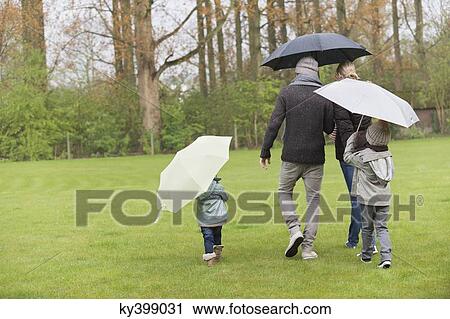 Stock Image - Family walking with umbrellas in a park. Fotosearch