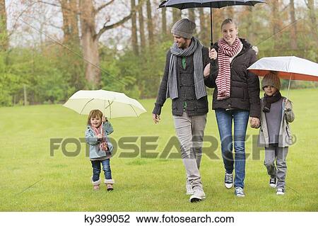 Stock Image - Family walking with umbrellas in a park. Fotosearch