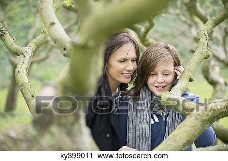 Stock Image - Woman with her daughter looking at a tree branch in an orchard. Fotosearch