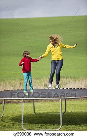 Woman with her son jumping on a trampoline in a field View Large Photo Image Stock Photo - Woman with her son jumping on a trampoline in a field. Fotosearch