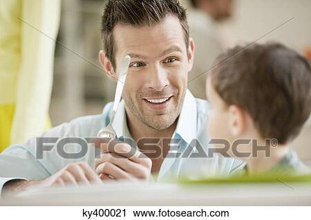 Stock Image - Man with his son sitting at a dining table. Fotosearch