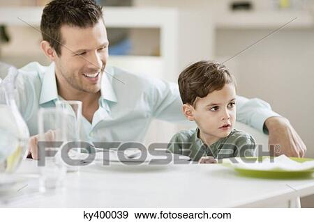 Man with his son sitting at a dining table View Large Photo Image Stock Photo - Man with his son sitting at a dining table. Fotosearch