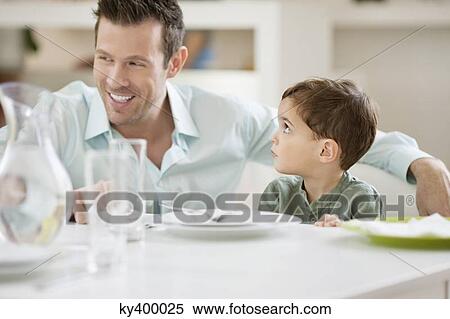Stock Photography - Man with his son sitting at a dining table. Fotosearch