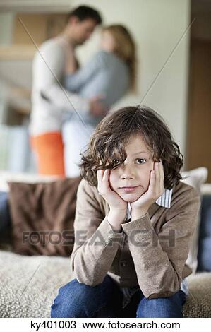 Stock Image - Boy sitting on a couch with his parents romancing in the background. Fotosearch