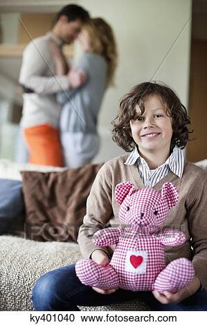 Boy sitting with a toy with his parents romancing in the background View Large Photo Image Stock Image - Boy sitting with a toy with his parents romancing in the background. Fotosearch
