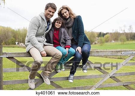 Stock Image - Boy sitting with his parents on the gate of a cottage. Fotosearch