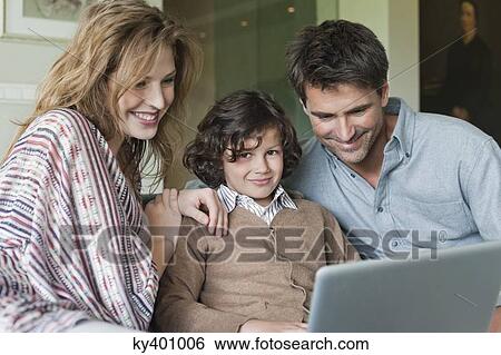 Stock Photograph - Boy using a laptop with his parents at home. Fotosearch