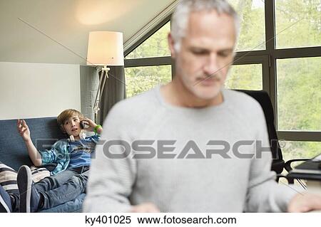 Stock Photography - Close-up of a man with his son talking on mobile phone in background. Fotosearch
