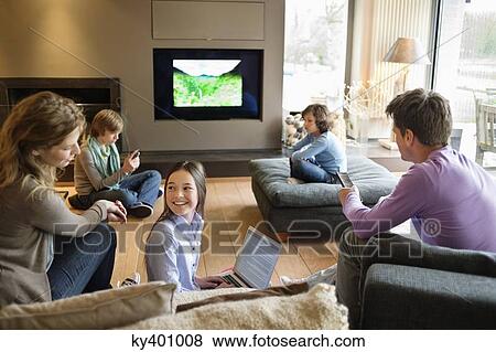 Family using electronic gadgets in a living room View Large Photo Image Stock Photo - Family using electronic gadgets in a living room. Fotosearch