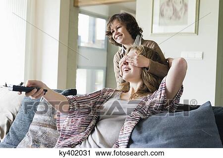 Boy covering his mother's eyes while watching TV View Large Photo Image Stock Image - Boy covering his mother's eyes while watching TV. Fotosearch