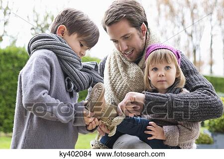 Picture - Boy putting shoe on his sister sitting in her father's lap. Fotosearch