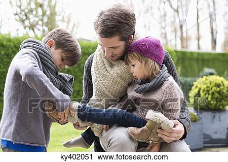 Boy putting shoe on his sister sitting in her father's lap View Large Photo Image Stock Image - Boy putting shoe on his sister sitting in her father's lap. Fotosearch