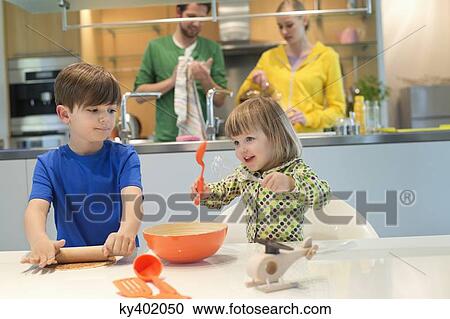 Stock Image - Children cooking in the kitchen with their parents in the background. Fotosearch
