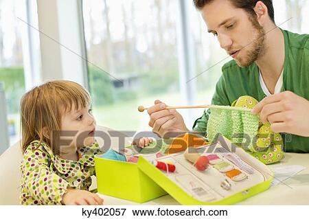 Stock Photo - Girl looking at her father knitting with wool. Fotosearch