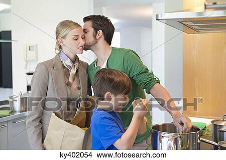 Man kissing his wife returning from shopping and son cooking in the kitchen View Large Photo Image Picture - Man kissing his wife returning from shopping and son cooking in the kitchen. Fotosearch