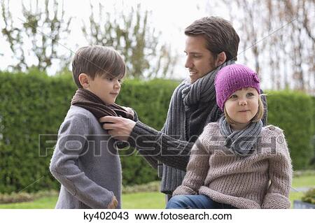 Stock Image - Man putting on warm clothing to his children. Fotosearch