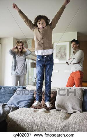 Naughty boy jumping on couch with his parents in the background View Large Photo Image Stock Photo - Naughty boy jumping on couch with his parents in the background. Fotosearch