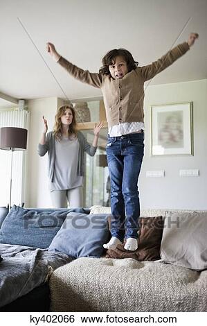 Naughty boy jumping on couch with his mother scolding him View Large Photo Image Stock Photograph - Naughty boy jumping on couch with his mother scolding him. Fotosearch